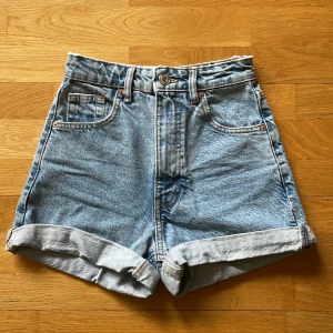 Högmidjade jeansshorts från Zara - Snygga ljusblå jeansshorts från Zara med hög midja och klassisk femficksdesign. Shortsen har uppvikta benslut, bälteshällor och knappstängning framtill. Perfekta för varma dagar och en chill streetstyle-look.