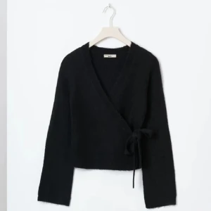 Svart omlottkofta med knyt - Svart omlottkofta med långa ärmar och knyt i sidan. Lite nopprig men annars bra skick, se bild 2 Koftan har en mjuk och mysig känsla, perfekt för lager-på-lager och chill dagar. Enkel och stilren design som funkar till många outfits.