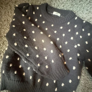 Grå stickad prickig tröja från JDY - Mysig grå stickad tröja från JDY med vita prickar över hela. Rund hals och långa ärmar med ribbade muddar. Perfekt för dig som gillar en chill och söt stil. Passar till jeans eller kjol och är superenkel att matcha.