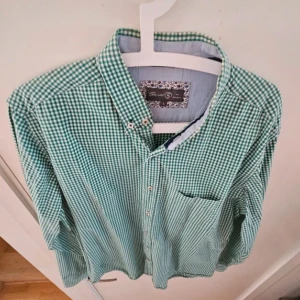 Grönvit rutig skjorta från Skill - Grön och vit rutig skjorta från Skill i storlek L. Klassisk button-down krage, bröstficka och vita knappar. Skjortan är långärmad och har en avslappnad passform. Perfekt för dig som gillar en stilren och tidlös look.