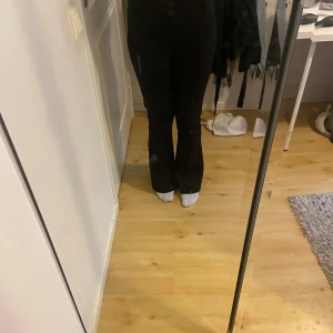 Svarta bootcut kostymbyxor från Gina Tricot - Säljer ett par svarta bootcut kostymbyxor från Gina Tricot i storlek M. Byxorna har hög midja, två knappar fram och snygga fickor med lock och knapp bak. Materialet är mjukt och stretchigt, perfekt för en chill och stilren look.