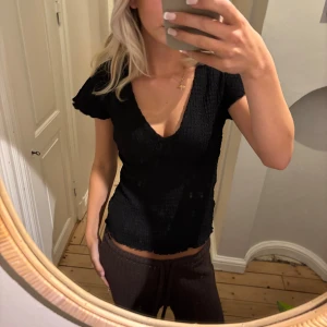 Svart smockad blus med volangärm - Supersöt svart blus med smockad struktur och v-ringning. Toppen har korta volangärmar och vågig kant nertill för en extra detalj. Sitter figurnära och använd ett fåtal gånger. Från newyorker storlek S!🩷