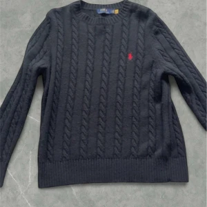Svart kabelstickad tröja från Polo Ralph Lauren - Säljer en stilren svart stickad tröja från Polo Ralph Lauren med kabelstickat mönster och röd broderad logga på bröstet. Tröjan är i fint skick. Vid några frågor eller fler bilder så är det bara att höra av sig.