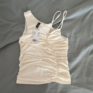Vit asymmetrisk linnetopp  - Supersnygg vit linnetopp från h&m med asymmetrisk design och smala axelband. Toppen har rynkade detaljer på ena sidan 