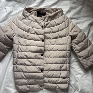 Beige trekvartsjacka från Guess - Snygg beige trekvartsjacka från Guess med trekvartsärm och rundad krage. Jackan har silverknappar och två fickor i fram. Enligt jackan är storleken xs, dock skulle jag påstå att den är lite större så närmare s/m beroende på hur tajt man vill ha den. Köpt förra säsongen men knappt använt. 