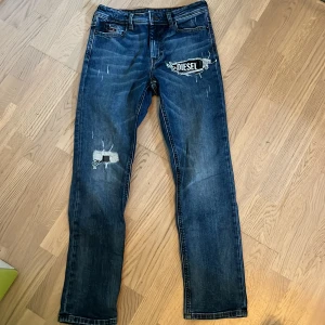 Blå jeans från Diesel - Snygga blå jeans från Diesel med coolt slitet utseende och en stor DIESEL-patch på ena låret. Dem är fin kvalité storlek S