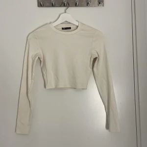 Krämvit croppad långärmad topp Zara - En stilren croppad långärmad topp från Zara i krämvit bomull. Enkel design med rund halsringning och tight passform. Superenkel att matcha och ett måste i garderoben.