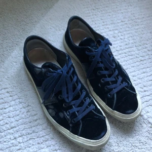 Mörkblå sammetssneakers från Tom Ford - Snygga sneakers från Tom Ford i mörkblå sammet med matchande blå snörning och vit sula. Klassisk låg modell med rund tå och diskret logga bak på hälen. Lyxig känsla med materialmix av sammet och skinn Nypris: ca 12 000 kr