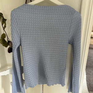 Ljusblå långärmad topp med vågig struktur - Supersöt ljusblå långärmad topp med vågig struktur i tyget och lätt utsvängda ärmar. Perfekt för dig som gillar unika detaljer och en chill vibe. Passar lika bra till jeans som kjol och är ett måste i garderoben för dig som vill sticka ut lite extra.