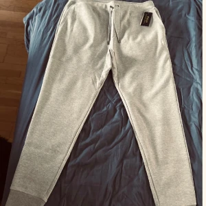 Grå mjukisbyxor Polo Ralph Lauren L - Snygga grå mjukisbyxor från Polo Ralph Lauren med klassisk logga broderad på benet. Byxorna har snörning i midjan, muddar vid bensluten och en bakficka. Perfekta för chill dagar eller när du vill vara bekväm men ändå se fräsch ut.
