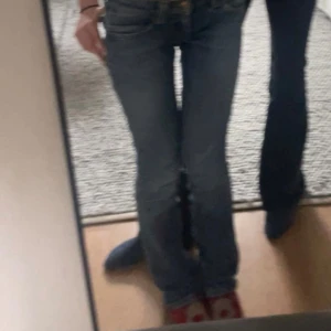 Blå bootcut jeans från Lee - Säljer ett par klassiska blå bootcut jeans från Lee med snygg slitning och låg midja. 