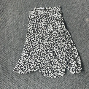 Blommig långkjol från Zara - Supersnygg svart långkjol från Zara med vitt blommönster. Kjolen har en flowy passform och är perfekt för dig som gillar en chill men ändå trendig stil. Tunn och lätt i materialet, vilket gör den skön att bära under varmare dagar. Tryck ej köp nu