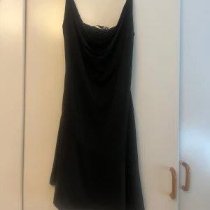 Svart kort klänning från NA-KD - Supersnygg svart kort klänning från NA-KD med draperad urringning och smala axelband. Aldrig använd och säljer pga för liten nu. 