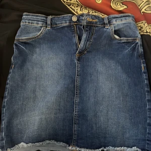 Blå jeanskjol från Pieces - Snygg blå jeanskjol från Pieces med rå kant nertill och klassiska fickor både fram och bak. Kjolen har normal passform, bälteshällor och dragkedja med knapp. Perfekt till sneakers eller boots för en chill look.