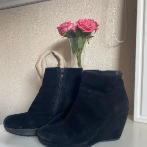 Svarta mocka kilklacksboots - Snygga svarta boots i mocka med kilklack och dragkedja på sidan. Skorna har en rund tå och en stilren design som passar perfekt till höst- och vinteroutfits. Perfekta för dig som vill ha lite extra höjd men ändå bekvämt. Storlek 40