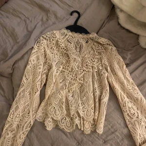 Beige spetsblus med volangdetaljer - Superfin beige blus i spets med långa ärmar från zara och snygga volangdetaljer framtill. Blusen har ett unikt mönster i spetsen och en lätt genomskinlig look som ger en romantisk vibe. Perfekt att styla med jeans eller kjol för en trendig outfit. PRIS KAN DISKUTERAS
