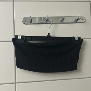 Svart ribbad bandeau tubtopp - Snygg svart bandeau tubtopp med ribbad struktur. Perfekt att styla med höga jeans eller kjol för en trendig look. Enkel och stilren design som passar till många outfits.