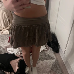 vikbar volangkjol med broderi - Supersöt brun kortkjol med volanger och broderade blommor som går att vika. Kjolen har bred midjeresår och fina virkade detaljer mellan volangerna. Perfekt för dig som gillar boho-stil och vill ha något unikt i garderoben. passar XS-M pågrund av elastiska bandet