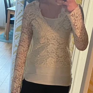 Beige spetsblus med lång ärm - Säljer en beige blus i genombruten spets med v-ringning och långa ärmar. Blusen har ett romantiskt mönster och är fodrad över kroppen men transparent på ärmarna. Perfekt för dig som gillar feminina detaljer och mjuka färger.