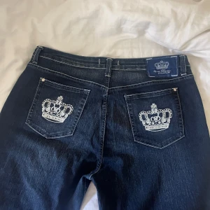 Victoria Beckham Rock & Republic jeans - Mörkblå jeans från Victoria Beckham for Rock & Republic med snygg broderad krona och strassdetaljer på bakfickan. Klassisk femficksmodell i 100% bomull, tillverkade i Italien. Perfekta för dig som vill sticka ut med exklusiva detaljer. Dem passar någon som är runt 160 i längden. 