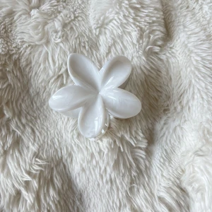 Vit blomformad hårklämma - Superfin hårklämma i form av en blomma med fem blad, helt i glansig vit plast. Perfekt accessoar för att ge en söt och fräsch touch till din frisyr. Klämman har en stabil metallfjäder och håller håret på plats hela dagen.