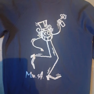 André x Mango M street art graffiti  - Säljer en blå sweatshirt från André x Mango i storlek M. Tröjan har ett stort vitt grafiskt tryck framtill med en tecknad figur och signatur. Klassisk rund halsringning och ribbade muddar. Perfekt för dig som gillar streetstyle och unika prints.