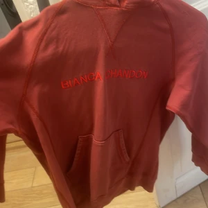 Röd hoodie från Bianca Chandôn - Säljer en röd hoodie från Bianca Chandôn med broderad logga på bröstet. Tröjan har huva med snörning, känguruficka och långa ärmar. Perfekt för dig som gillar streetwear och vill ha något snyggt och bekvämt.