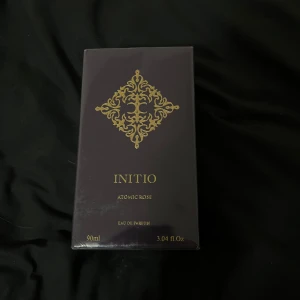 Initio Atomic Rose Eau de Parfum 90ml - Lyxig parfym från Initio, Atomic Rose, 90ml Eau de Parfum. Förpackningen är mörklila med eleganta gulddetaljer och exklusiv design. Tillverkad i Frankrike och levereras i en stilren, fyrkantig kartong. Perfekt för dig som gillar unika och intensiva dofter.