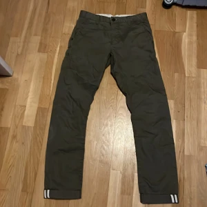 Mörkgröna chinos med vita detaljer från Zara - Snygga mörkgröna chinos med raka ben och vita ränder på bensluten. Klassisk passform med fickor fram och bak, perfekta för en clean och avslappnad stil. Tillverkade i bomull för skön känsla hela dagen.