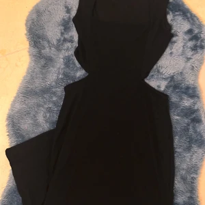 Svart långklänning från Gina Tricot - Snygg svart långklänning från Gina Tricot med cut out-detaljer i midjan. Klänningen är ärmlös och har en tight passform med rundad halsringning. Materialet är ribbat och stretchigt, vilket ger en bekväm och smickrande siluett. Du kan hitta mer på min sida.