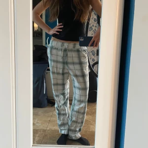 Rutiga mjukisbyxor/pyjamasbyxor med snörning - Superbekväma mjukis eller pyjamasbyxor i vitt och ljusgrönt rutigt mönster. De har elastisk midja med snörning och raka ben. Perfekta för chill dagar hemma eller när du vill vara extra comfy.
