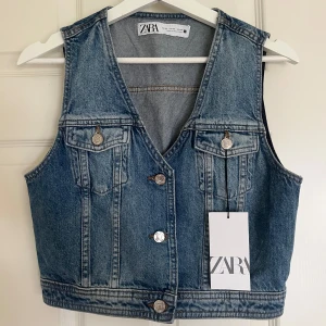 Blå jeansväst från ZARA - Trendig blå jeansväst från ZARA med klassisk v-ringning och knappar framtill. Västen har två bröstfickor med lock och silverfärgade knappar. Snygg tvättad denimlook och croppad passform som ger en cool vibe till din outfit. Aldrig använd & skickas inom 1-2 dagar💙