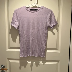 Ljuslila ribbad topp  - Säljer en ljuslila ribbad topp från 157 med korta ärmar och vågig kant vid ärmslut och nederkant.