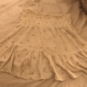 Vit blommig volangkjol från 157 - Supersöt vit kortkjol från 157 med små blommor i pastellfärger. Kjolen har några fina volanger.