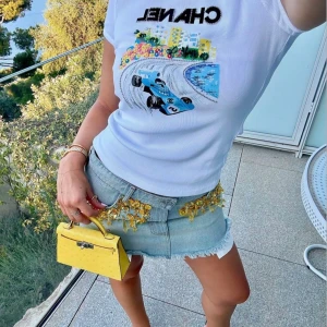 Snygg topp  - Perfekt till sommaren, helt ny och oanvänd. Sitter tight på kroppen och är enkel att styla. Köptes för 1500kr . Populär modell, identiskt med den äkta (går att googla) först till kvarn🥰.                          Vit t-shirt  med coolt tryck av en blå racerbil, färgglada blommor och paljettdetaljer. Stor svart logga framtill. Tight passform och korta ärmar, perfekt för dig som gillar statement-plagg.