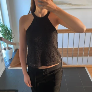Svart spetsig topp Gina Tricot - Supersnygg svart topp från Gina Tricot i spets. Toppen är ärmlös och har knytning i nacken med ett brett satinband. Den är i bra skick!!💕🥰