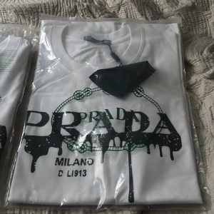 Vit PRADA t-shirt med  - Vit t-shirt från PRADA med coolt svart tryck framtill där loggan ser ut att smälta. Klassisk rund halsringning och korta ärmar. Perfekt för dig som gillar streetstyle och vill sticka ut med en designerpiece. Priset kan diskuteras vid snabb affär. Säljs gärna snabbt då ja reser om några dagar.