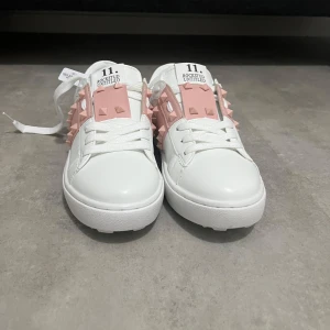 Valentino Rockstud sneakers vit/rosa - Snygga vita Valentino Rockstud sneakers med rosa detaljer och ikoniska nitar. Den är helt ny och oanvänd i storlek 37 och passar perfekt för dig som söker en fräsch och stilig look. 
