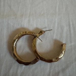 Guldiga örhängen - Säljer ett par chunky guldiga med hamrad yta. De är runda och har en cool, lite ojämn finish som ger dem extra edge. Perfekta för att lyfta vilken outfit som helst!