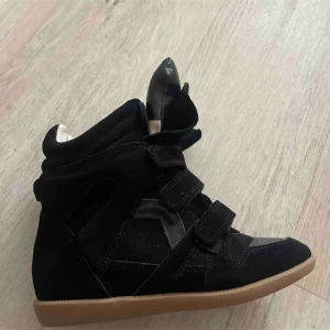 Svarta sneakers i mocka med kardborre - Snygga svarta sneakers i mocka med cool design och högt skaft. Skorna har flera kardborreband och en brun platt sula. Perfekta för dig som vill ha en sportig och trendig look med extra edge. Kom gärna med pris förslag!