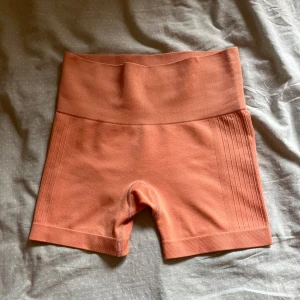 Korta seamless träningsshorts WORK OUT - Snygga seamless träningsshorts från WORK OUT i en varm, ljus orange färg. Hög midja och ribbade detaljer längs sidorna ger en sportig vibe. Perfekta för gymmet eller löprundan, tillverkade i mjukt och stretchigt polyestermaterial för maximal komfort.