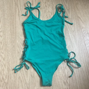 Turkos baddräkt med snörning H&M - Snygg turkos/grön baddräkt från H&M i storlek 36 (passar mer som 34). Modellen har smala axelband som knyts och cool snörningsdetalj längs båda sidorna. Perfekt för stranden eller poolen, med en enkel men trendig look. Materialet är stretchigt och bekvämt syntet.
