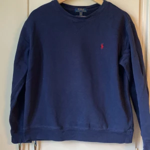 Ralph Lauren marinblå tröja - mörkblå sweatshirt från Polo Ralph Lauren med röd broderad logga på bröstet. Tröjan har rund halsringning och långa ärmar. Tillverkad i mjuk bomull. Storlek 14-16 men ålder 12-15