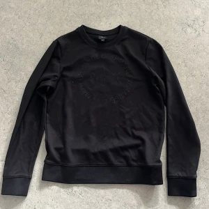 Svart sweatshirt från Armani Exchange - Svart sweatshirt från Armani Exchange med rund hals och diskret logga i svart ton på bröstet. Tröjan har långa ärmar, breda muddar och är tillverkad i mjuk bomullsmix. 
