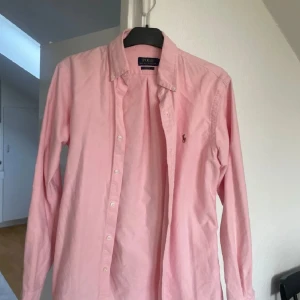 Rosa skjorta från Polo Ralph Lauren - Snygg rosa skjorta från Polo Ralph Lauren i slim fit-modell. Klassisk button down-krage, långa ärmar och broderad logga på bröstet. Skjortan är i bomull och har knäppning framtill. Perfekt för dig som gillar stilrena och tidlösa plagg. 100% äkta✅ inga defekter. Pris kan diskuteras😊