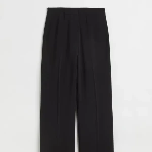 Svarta vida kostymbyxor - Snygga svarta kostymbyxor med hög midja och vida ben. Byxorna har en klassisk look med pressveck och är perfekta för en clean och stilren outfit. Tillverkade i ett mjukt material som ger en skön känsla hela dagen.