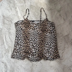 Topp - Säljer en snygg leopardmönstrad linnetopp från Gina Tricot i storlek XL. Toppen har tunna axelband och är i ett lätt, mjukt material. Perfekt för dig som vill sticka ut med ett djurmönster och gillar en avslappnad men trendig look.