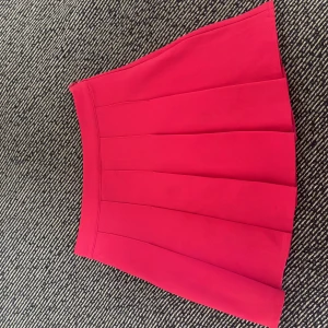 Rosa kjol från NewYorker - Superfin rosa kortkjol från NewYorker med plisserad design. Kjolen har hög midja och är gjord i ett mjukt, lite stretchigt material som sitter snyggt. Perfekt för sommaren eller en utklädnad för halloween. Är endast använd en gång under halloween. 