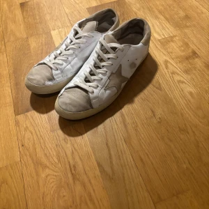GGDB Superstar sneakers med stjärndetalj - Snygga GGDB Superstar sneakers i vitt skinn med beige mockadetaljer och ikonisk stjärna på sidan. Skorna har snörning, platt sula och svart yttersula. Perfekta för dig som gillar en avslappnad och trendig look.