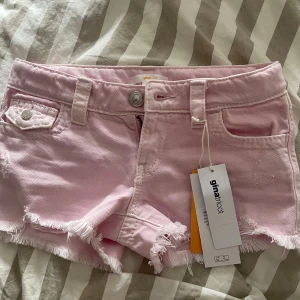 Ljusrosa lågmidjade jeansshorts från Gina Tricot - Snygga ljusrosa jeansshorts från Gina Tricot med fransig kant och klassiska fickor både fram och bak. Shortsen har bälteshällor, knapp och dragkedja framtill samt coola detaljer som råa kanter. Perfekta för sommardagar och festivalhäng. Säljer för att de inte passar🫰🏼